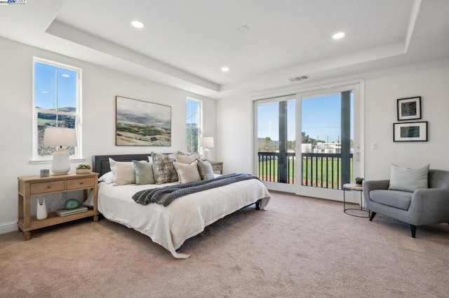 carpeted bedroom with access to outside and a tray ceiling