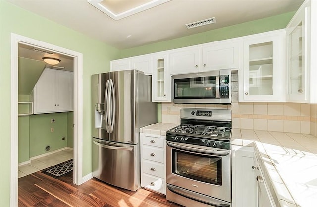 kitchen with backsplash, stainless steel appliances, dark hardwood / wood-style floors, white cabinets, and tile countertops