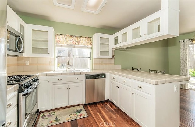 kitchen featuring white cabinetry, tile countertops, kitchen peninsula, and appliances with stainless steel finishes