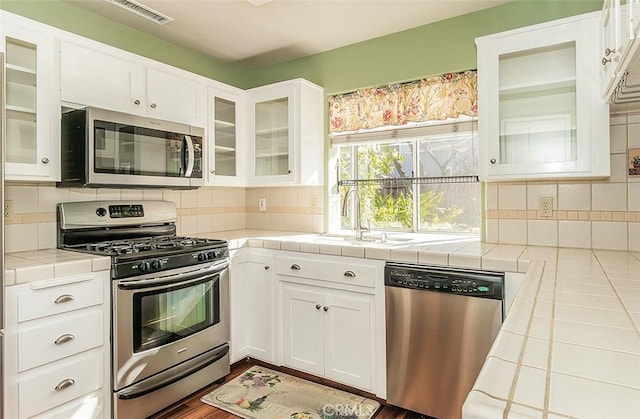 kitchen featuring sink, white cabinetry, tasteful backsplash, appliances with stainless steel finishes, and tile counters