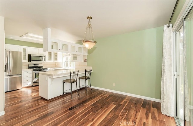 kitchen with appliances with stainless steel finishes, white cabinetry, dark hardwood / wood-style flooring, a kitchen bar, and kitchen peninsula