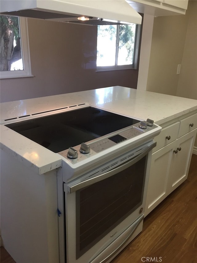 kitchen featuring white cabinets, dark hardwood / wood-style flooring, light stone countertops, wall chimney range hood, and electric stove