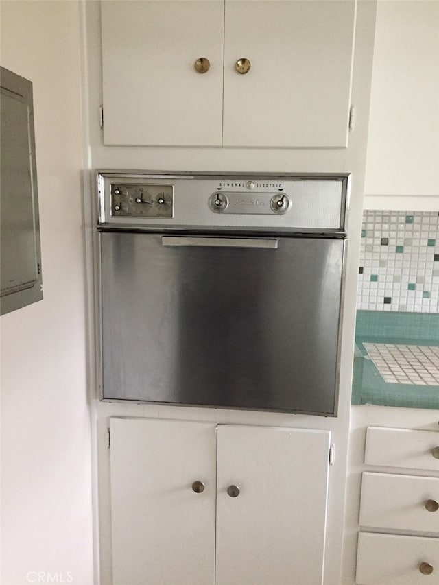 room details featuring white cabinetry, electric panel, and oven