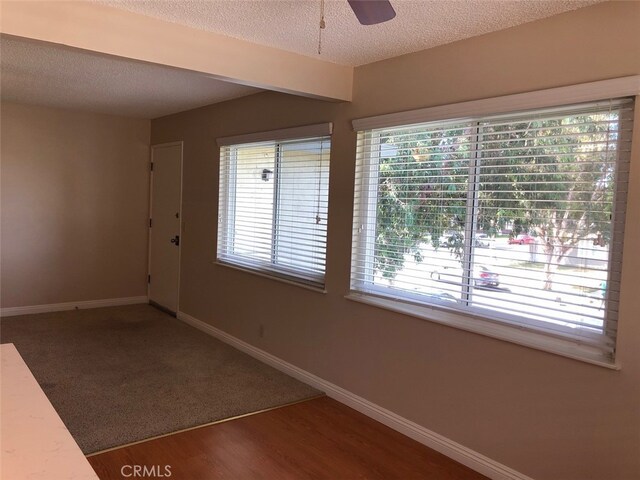 empty room with ceiling fan, a wealth of natural light, a textured ceiling, and dark hardwood / wood-style flooring