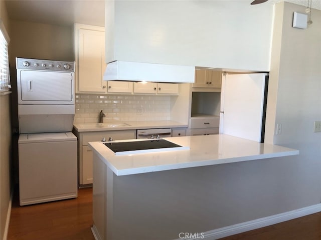 kitchen featuring sink, decorative backsplash, stacked washer and dryer, white fridge, and black electric cooktop