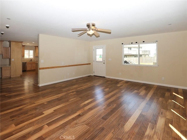 unfurnished living room featuring dark wood-type flooring, a sink, baseboards, and a ceiling fan