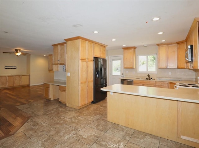 kitchen featuring a peninsula, a sink, light countertops, appliances with stainless steel finishes, and light brown cabinetry