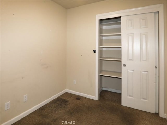 unfurnished bedroom featuring a closet, dark carpet, and baseboards