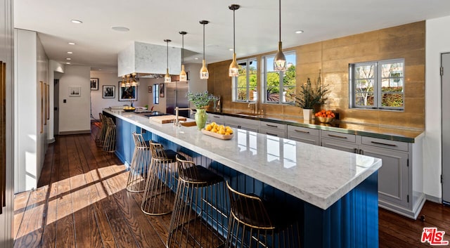 kitchen featuring pendant lighting, tasteful backsplash, an island with sink, and high end fridge