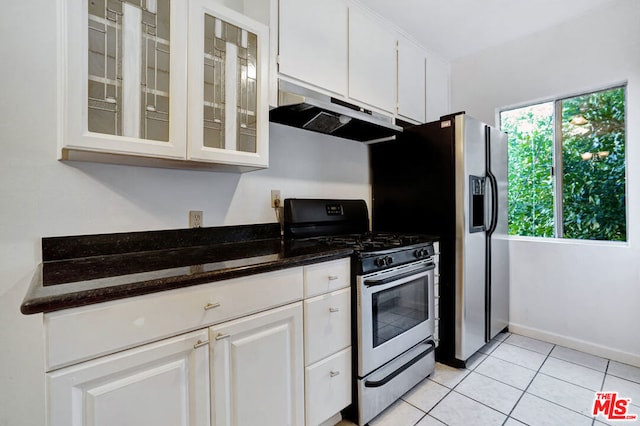 kitchen with stainless steel appliances, white cabinetry, light tile patterned floors, and dark stone counters