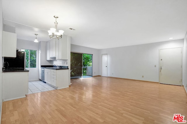 kitchen featuring a notable chandelier, light hardwood / wood-style floors, white cabinets, black fridge, and decorative light fixtures