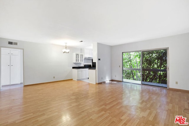 unfurnished living room with a notable chandelier and light wood-type flooring