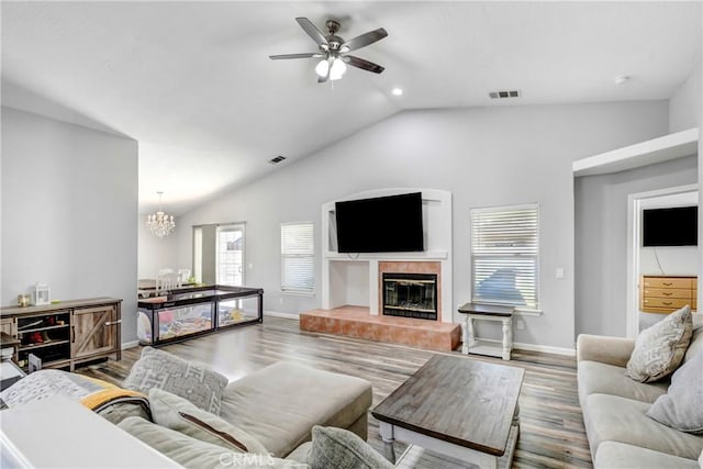 living room with a tile fireplace, wood-type flooring, vaulted ceiling, and ceiling fan with notable chandelier