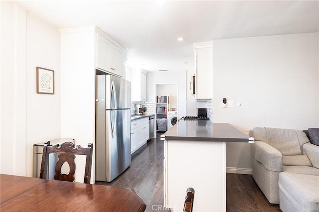 kitchen with appliances with stainless steel finishes, white cabinets, dark hardwood / wood-style flooring, washer / dryer, and kitchen peninsula