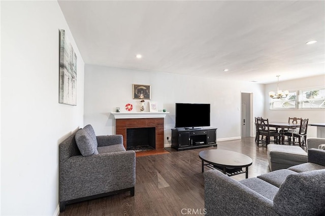 living room with a brick fireplace, dark wood-type flooring, and a chandelier