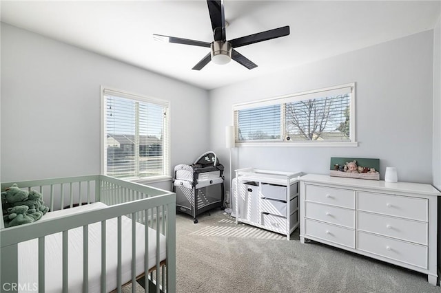 carpeted bedroom featuring a nursery area and ceiling fan