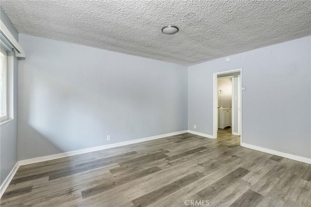 unfurnished room with a textured ceiling, wood finished floors, and baseboards