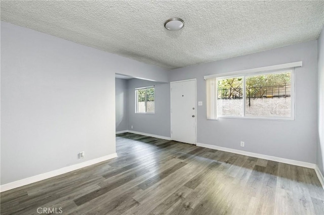 empty room featuring a textured ceiling, baseboards, and wood finished floors