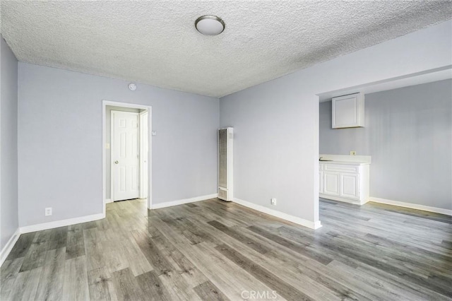 unfurnished room with a textured ceiling, baseboards, and wood finished floors