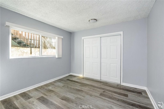 unfurnished bedroom featuring a textured ceiling, a closet, wood finished floors, and baseboards