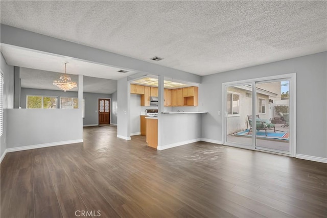 unfurnished living room with an inviting chandelier, dark hardwood / wood-style floors, and a textured ceiling