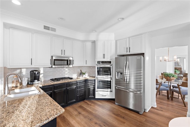 kitchen featuring appliances with stainless steel finishes, white cabinets, backsplash, sink, and an inviting chandelier