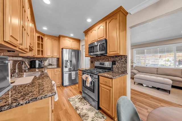 kitchen featuring sink, light hardwood / wood-style flooring, dark stone countertops, appliances with stainless steel finishes, and backsplash