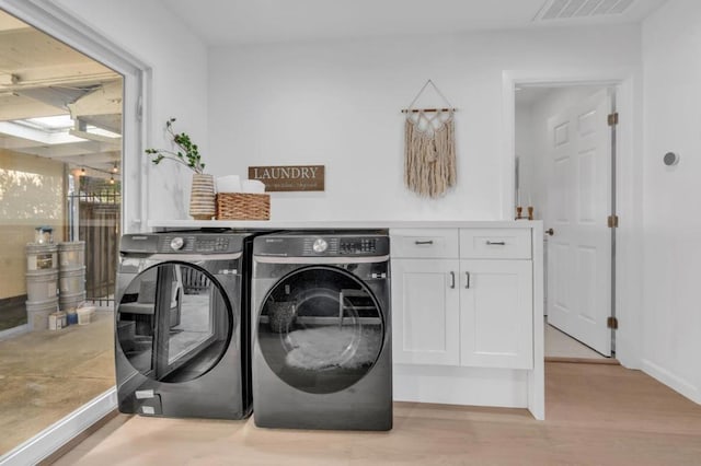 clothes washing area with cabinets, separate washer and dryer, and light hardwood / wood-style flooring