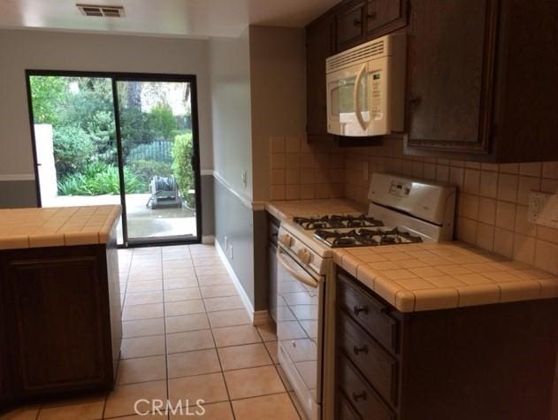 kitchen featuring tasteful backsplash, white appliances, tile counters, and dark brown cabinets