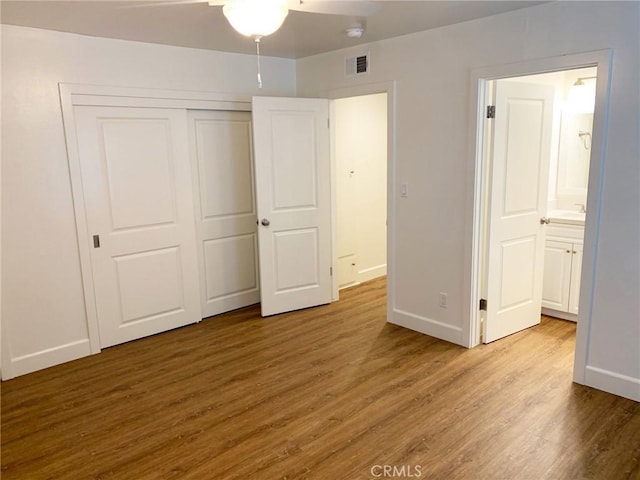 unfurnished bedroom featuring hardwood / wood-style flooring, ensuite bath, a closet, and ceiling fan