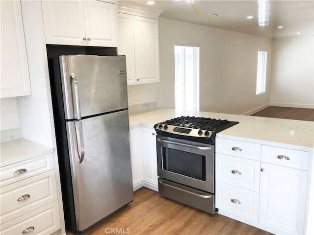 kitchen featuring light hardwood / wood-style flooring, appliances with stainless steel finishes, kitchen peninsula, a healthy amount of sunlight, and white cabinets