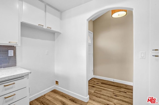 kitchen with decorative backsplash, light stone countertops, white cabinets, and light wood-type flooring