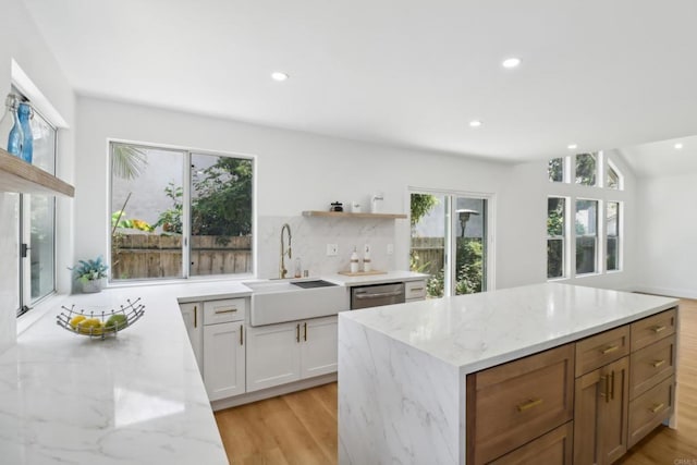 kitchen with sink, white cabinets, stainless steel dishwasher, light stone countertops, and light hardwood / wood-style flooring