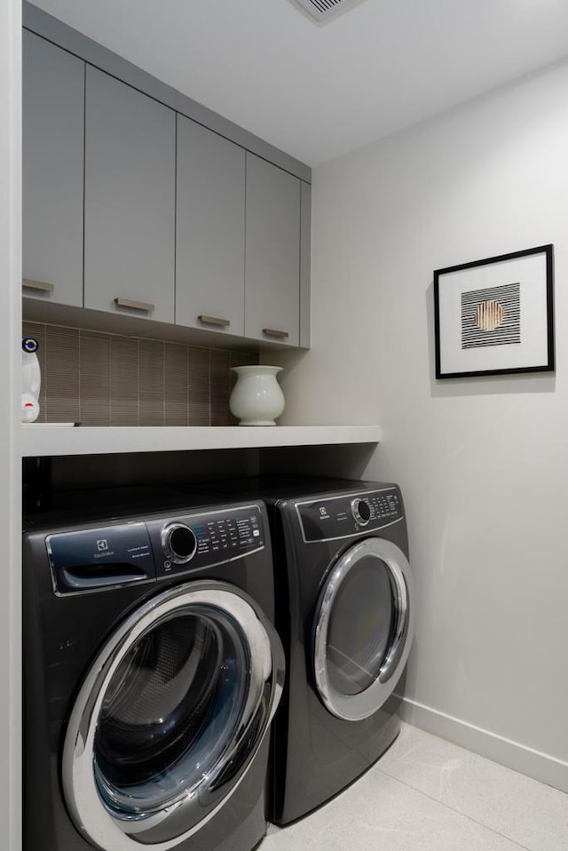 clothes washing area featuring cabinets, washer and clothes dryer, and light tile patterned floors