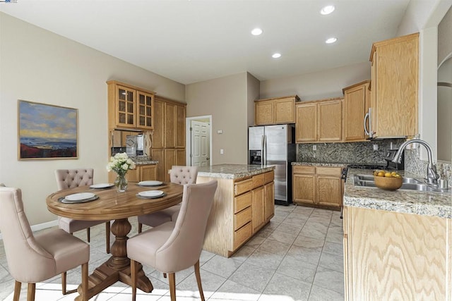 kitchen with sink, light stone counters, a center island, stainless steel appliances, and decorative backsplash