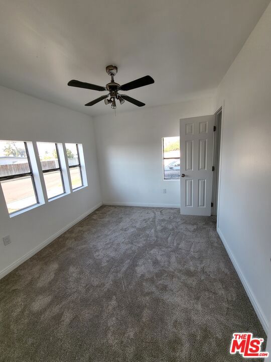 unfurnished room with dark colored carpet and ceiling fan