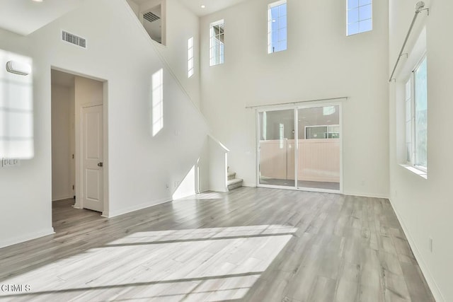 unfurnished living room featuring a towering ceiling and light hardwood / wood-style flooring