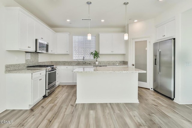 kitchen featuring appliances with stainless steel finishes, a center island, white cabinets, and decorative light fixtures