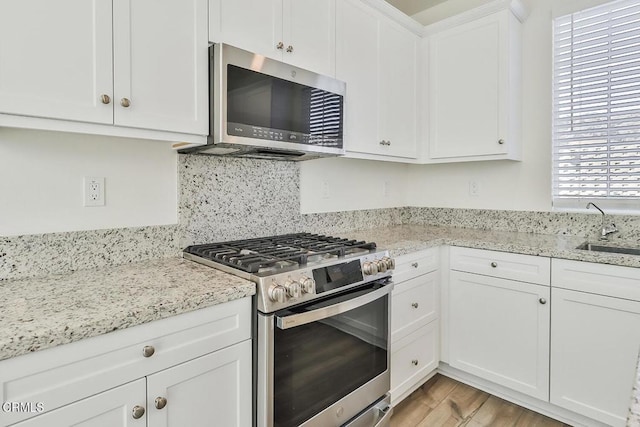 kitchen with sink, stainless steel appliances, light hardwood / wood-style floors, light stone countertops, and white cabinets