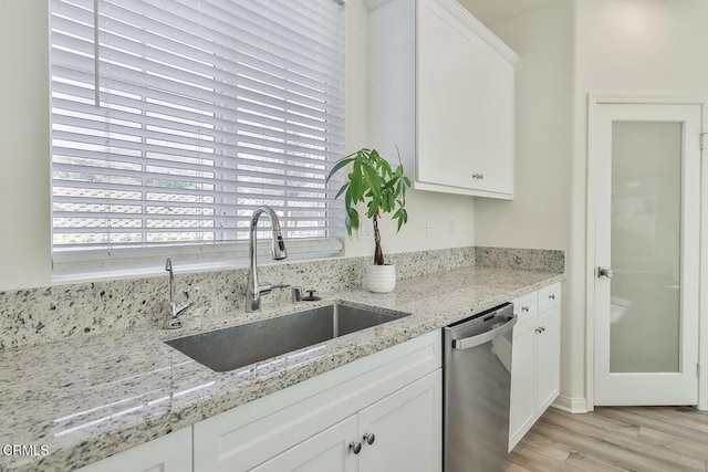 kitchen with sink, stainless steel dishwasher, light stone countertops, light hardwood / wood-style floors, and white cabinets