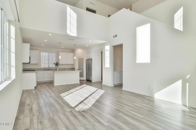 kitchen featuring white cabinetry, a center island, a high ceiling, stainless steel fridge with ice dispenser, and decorative light fixtures