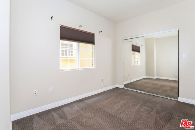 unfurnished bedroom featuring dark carpet and a closet