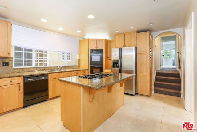 kitchen featuring a breakfast bar, a center island, black appliances, stone countertops, and decorative backsplash