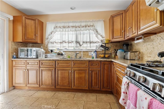 kitchen featuring sink, gas range, ventilation hood, light stone countertops, and decorative backsplash