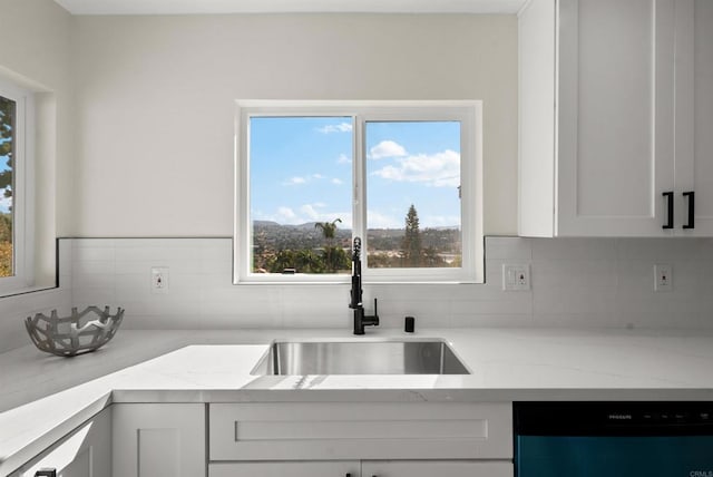 kitchen with light stone counters, sink, white cabinets, and dishwasher