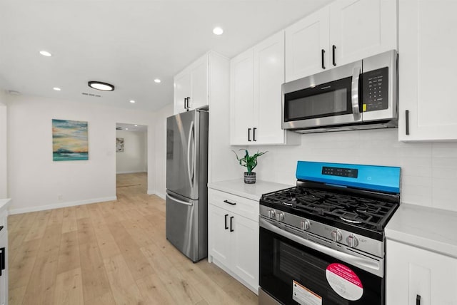 kitchen featuring tasteful backsplash, light wood-type flooring, appliances with stainless steel finishes, light stone countertops, and white cabinets