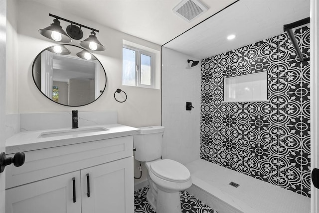 bathroom with tiled shower, vanity, and toilet