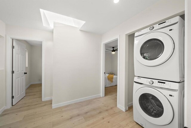 clothes washing area featuring a skylight, stacked washer and clothes dryer, and light wood-type flooring