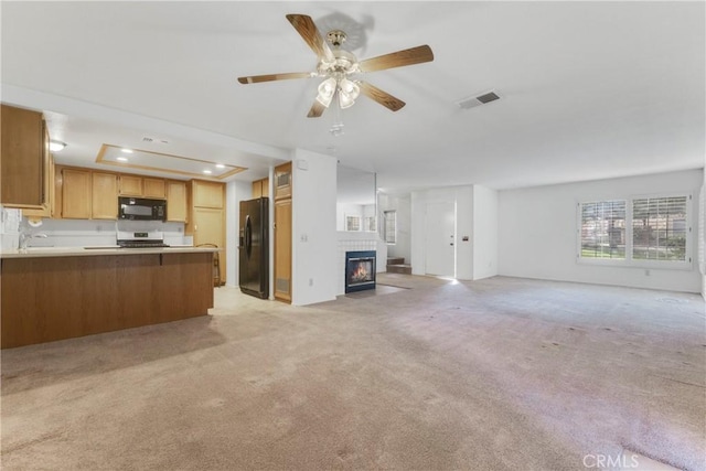 kitchen with ceiling fan, a tray ceiling, black appliances, light colored carpet, and kitchen peninsula