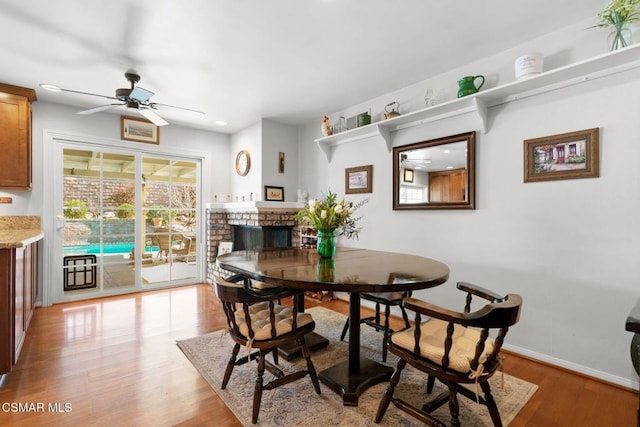 dining room with a fireplace, ceiling fan, and light wood-type flooring